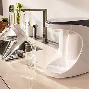 AquaTru&reg; on a kitchen counter with crystal clear water in a glass